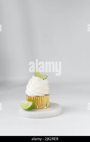 Cupcake de citron vert sur une assiette avec d'autres cupcakes en arrière-plan, cupcake de margarita avec crème blanche de beurre et un coin de lime, cupcake de margarita Banque D'Images