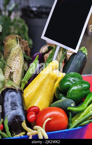 Un panier de tomates fraîches de la ferme, de poivrons, d'aubergines et de maïs. Un petit signe vierge avec un champ noir est en place pour le texte supplémentaire. Banque D'Images