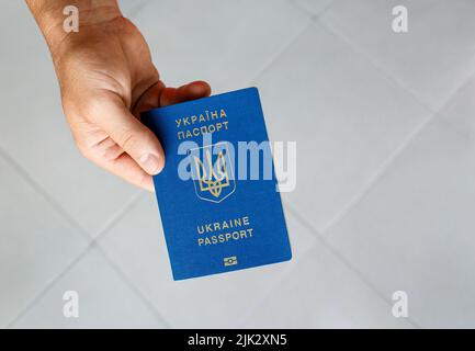 Passeport d'un citoyen ukrainien dans une main mâle sur fond gris, gros plan. Banque D'Images