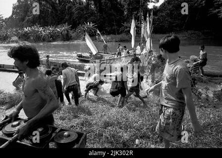 Kalimantan occidental, Indonésie. Mars 2007. Un homme décharge un jeu d'instrument de percussion gamelan, alors qu'il passe devant une foule de gens - la communauté Dayak Tamambaloh - qui s'éclaboussent de l'eau les uns sur les autres comme un acte purifiant, devant un bateau qui vient de transporter la famille de leur nouveau chef traditionnel pour une visite au lieu de sépulture de leur ancien chef dans le village de Sungai Uluk Palin (Sungulo Palin), Putusibau Utara, Kapuas Hulu, West Kalimantan, Indonésie. La culture est un élément indispensable de tout développement, selon l ' Organisation des Nations Unies. Banque D'Images