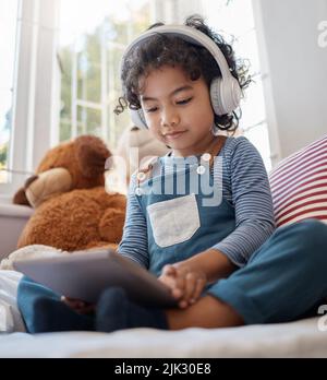 Nous sommes leur héritage. Un adorable jeune garçon utilisant une tablette numérique et un casque dans sa chambre à la maison. Banque D'Images