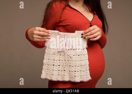 Une femme enceinte tient dans ses mains la robe d'un enfant Banque D'Images