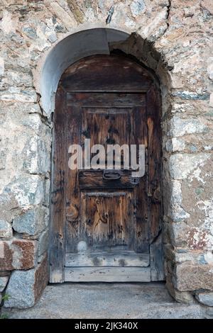 Ancienne porte en bois aux intempéries avec plaques de verrouillage rouillées et poignée dans un mur, massée de grandes pierres naturelles Banque D'Images