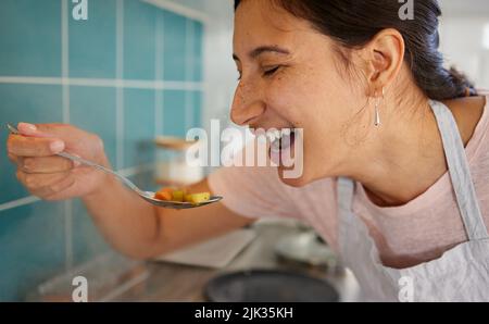 Je pense que c'est bon. Une jeune femme goûtant sa nourriture. Banque D'Images