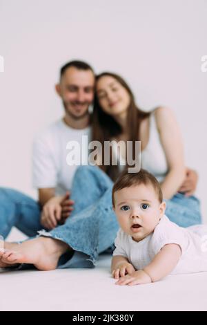 Vue latérale de bébé bébé enfant en couches et body blanc est rampant sur tous les quatre avec ses jambes dehors, essayant de se tenir debout regardant l'appareil photo au-dessus de wh Banque D'Images