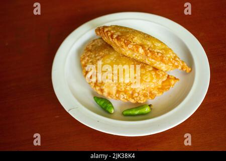 gâteau de pasties ou gâteau de pâtisserie ou kue pastel servi avec du piment vert dans une petite assiette sur fond de bois. gâteau indonésien pastel Banque D'Images