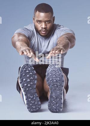 Préparer ces muscles au travail. Prise de vue en longueur d'un beau jeune homme assis et s'étirant dans le studio. Banque D'Images