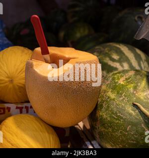 Couper le melon avec un couteau coincé dans le fond des pastèques sur le marché pour la vente Banque D'Images