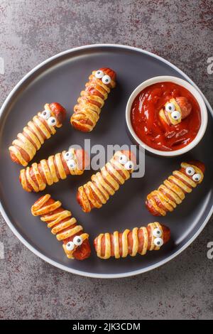 Momie saucisse dans la pâte effrayante Halloween nourriture de vacances avec les yeux drôles et la sauce sur une assiette sur la table. Vue verticale du dessus Banque D'Images