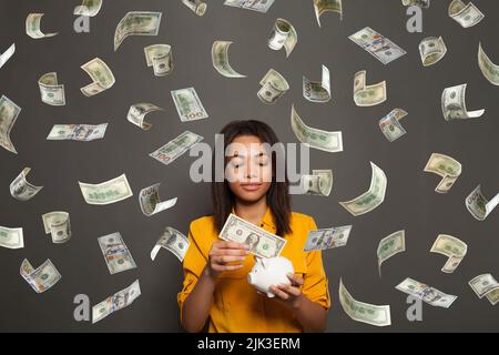 Une femme intelligente et réussie tenant une banque d'argent sur un fond noir, en train de baisser l'argent du dollar américain Banque D'Images