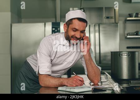 Chef souriant en uniforme en ordre pour le fournisseur debout sur la cuisine Banque D'Images