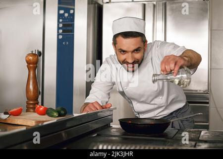 Le chef professionnel verse de l'huile dans une poêle pour préparer le plat dans la cuisine du restaurant Banque D'Images