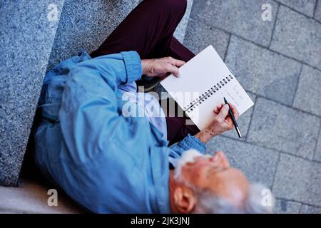 Vue de dessus d'un homme senior assis à l'extérieur et écrivant à la liste des tâches. Banque D'Images