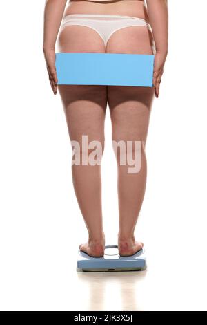 Vue arrière d'une femme obèse debout sur une balance et tenant une planche vide derrière elle Banque D'Images