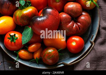 Tomates de différentes variétés et tailles sur un plateau en fer sur une table en bois. Banque D'Images