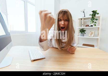 Une femme d'affaires blonde méchante en colère hurlant devant ses subordonnés en se secouant le poing devant la caméra, assis sur son lieu de travail dans un bureau moderne. Le directeur irrité travaille sur Banque D'Images
