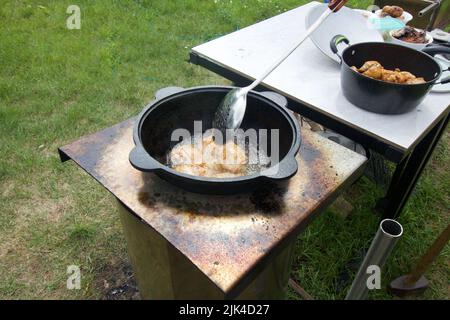 Les cuisses de poulet sont frites dans un chou-fleur en fonte. Il y a de la fumée et de la vapeur. À proximité, vous trouverez des frites. Cuisiner à l'extérieur. Gros plan. Banque D'Images