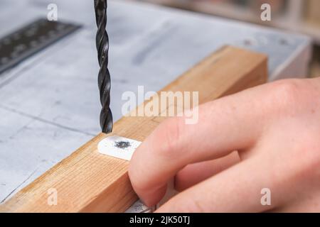 Un homme fore des trous dans un crochet en fer avec une perceuse pour accrocher un écran en bois sur une batterie. Banque D'Images