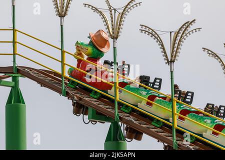 Montagnes russes. Enfants sur une montagne à roulettes avec un personnage de dessin animé crocodile voiture principale. Isolé sur fond ciel clair. Crème verte, Banque D'Images