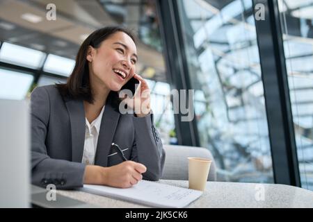 Jeune femme d'affaires chinoise gaie qui parle au téléphone et qui travaille au bureau. Banque D'Images