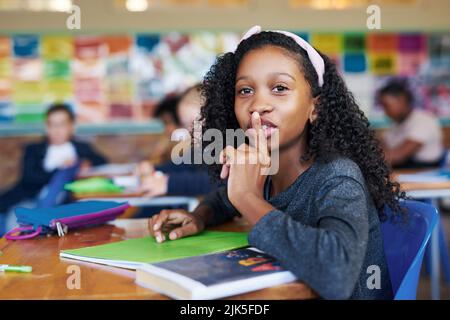 SHH, vous n'êtes pas censé parler. Une jeune fille assise dans sa salle de classe avec son doigt sur ses lèvres dans un geste de précipitation. Banque D'Images