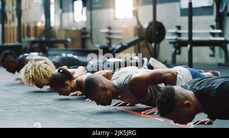 Poussez-vous un peu plus à chaque fois. Un groupe de jeunes sportifs faisant des poussettes ensemble dans une salle de sport. Banque D'Images