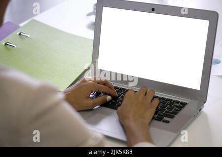 Vue arrière d'une femme d'affaires en costume s'asseoir au bureau dans le bureau dactylographiant sur ordinateur portable clavier avec écran blanc. Banque D'Images