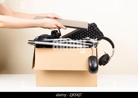 Les mains des femmes mettent l'ordinateur portable ancien dans une boîte en carton plein d'ordinateurs et de gadgets utilisés pour le recyclage. Obsolescence planifiée, e-déchets, dons Banque D'Images