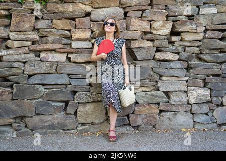 Femme mûre se penchée sur un mur de pierre et se ventilant par la forte chaleur estivale. Banque D'Images