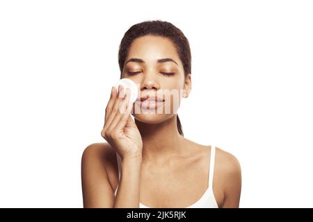 Jeune belle afro-américaine femme nettoyant son visage du maquillage avec des tampons de coton blanc sur fond blanc Banque D'Images