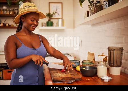 Quelqu'un m'épouse déjà. Une jeune belle femme portant un chapeau de soleil tout en coupant des fruits dans la cuisine à la maison. Banque D'Images