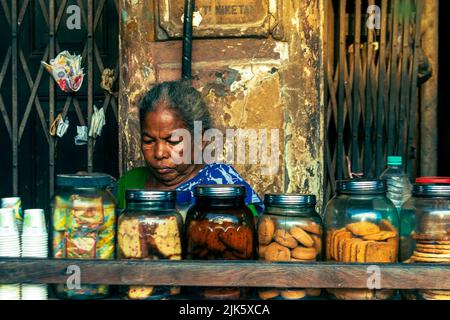 Kolkata, Inde - 9 juillet 2022: Portrait d'une vendeuse de thé âgée assise sous un vieux bâtiment avec une variété de biscuits conservés devant. Sélectif Banque D'Images