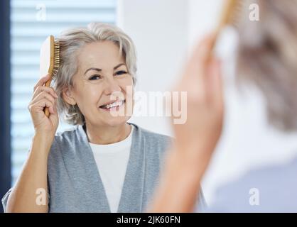 Gris sûr semble bien sur moi. Une femme âgée se brossant les cheveux tout en regardant dans son miroir de salle de bains. Banque D'Images