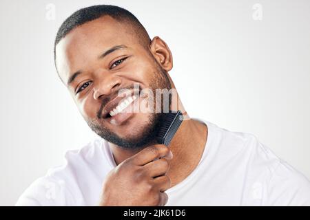 Une routine quotidienne de toilettage aide à maintenir votre hygiène personnelle. Portrait studio d'un jeune homme beau brossant sa barbe sur un blanc Banque D'Images