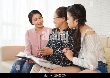 Femme asiatique senior montrant un album avec de vieilles photos à sa fille et sa petite-fille Banque D'Images