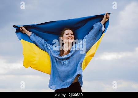 Une femme ukrainienne gratuite heureuse avec drapeau national sur fond de ciel spectaculaire. Portrait de dame en bleu broderie vyshyvanka chemise. Ukraine, indépendance Banque D'Images