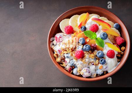 Petit-déjeuner au granola avec yaourt, myrtille, framboise, banane et pêche. Petit déjeuner sain avec yaourt, granola cuite au four et fruits sur une assiette en argile. Top vie Banque D'Images