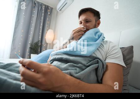 Un jeune homme avec un mal de gorge et un nez qui coule se trouve dans le lit Banque D'Images