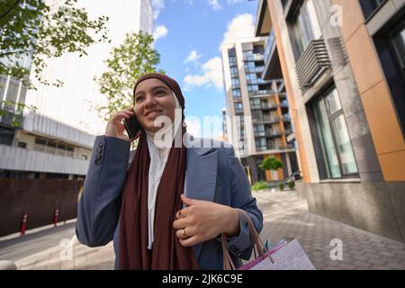 Une femme arabe avec des paquets marche dans la rue et parle au téléphone Banque D'Images