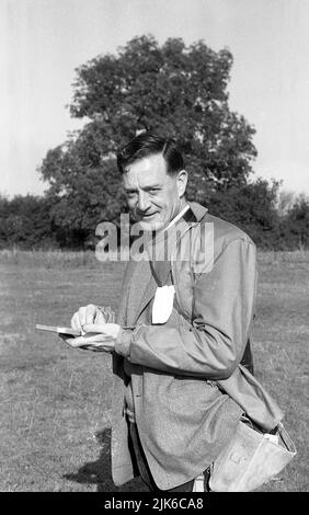 1960s, historique, en plein air, un pêcheur grossier, tenant un petit plateau à la recherche d'un crochet, Angleterre, Royaume-Uni. Vêtements de pêche de l'époque, sac à bandoulière en toile, veste imperméable et pull sur une veste de sport. Banque D'Images