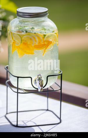 Bouteille, pot de limonade à l'orange et au citron maison. Un grand conteneur avec robinet est placé sur une table de fête lors d'un pique-nique, d'une fête. Mise au point sélective, flou b Banque D'Images