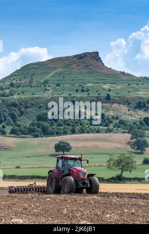 Tracteur McCormick cultivant un lit de semence sur le bord des Moors de North York, avec une garniture de roseberry en arrière-plan. Yorkshire, Royaume-Uni. Banque D'Images