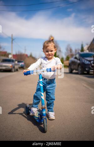 Adorable petite fille en combinaison bleue sur un scooter de kick. Bonne santé bébé adorable enfant s'amuser dans la ville. Enfant actif par temps froid Banque D'Images