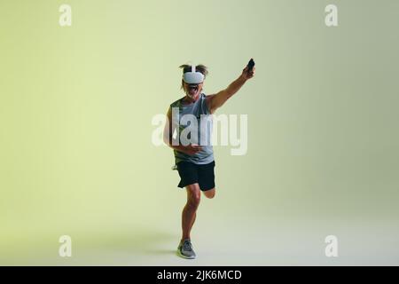 Homme senior joyeux gagnant un jeu de fitness de réalité virtuelle dans un studio. Homme sportif senior célébrant sa victoire tout en portant une réalité virtuelle lui Banque D'Images
