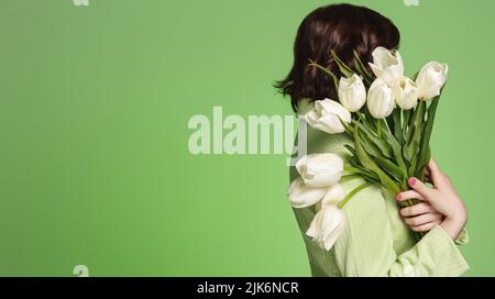 Silhouette de jeune femme tenant un bouquet de tulipes blanches. La fille tient de belles fleurs, porte une veste, se tient sur fond vert Banque D'Images