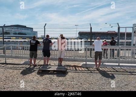 Un groupe de personnes se tenant le long de la piste de course regardant les voitures de course passer au Mans Banque D'Images