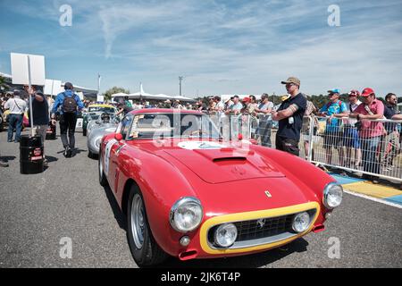 Un pilote se prépare à l'intérieur d'une voiture de course classique rouge Ferrari avant une course au Mans alors que son coéquipier est debout à côté de la voiture Banque D'Images