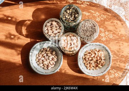 Noix de cajou, pistaches, graines de tournesol et graines de citrouille dans des pots en verre et un bol en porcelaine sur la table. Des collations saines Banque D'Images