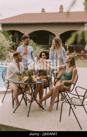 Groupe de jeunes heureux qui applaudissent au cidre près de la piscine dans le jardin Banque D'Images