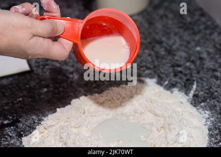 femme versant du lait sur un mélange de farine et de beurre pour préparer un gâteau Banque D'Images